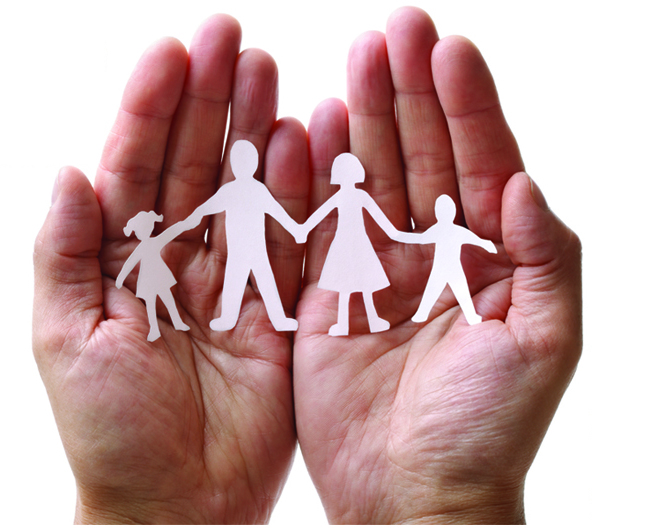 Photo of two open hands holding a paper cut-out of a family holding hands in a line.