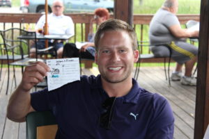 Photo of golfer holding up a piece of paper with an X next to "Closest to Pin"