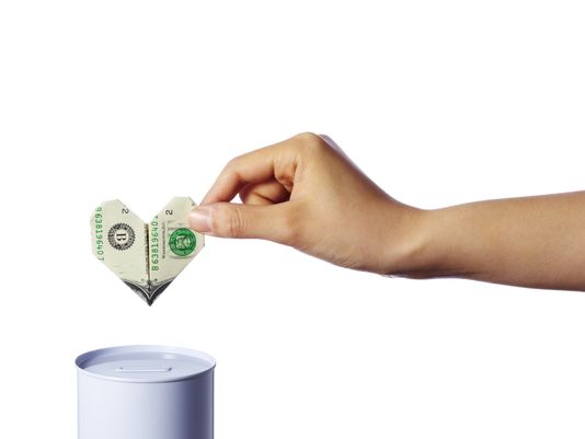 Photo of a person dropping an origami-folded heart-shaped dollar bill into a jar, representing charitable giving.
