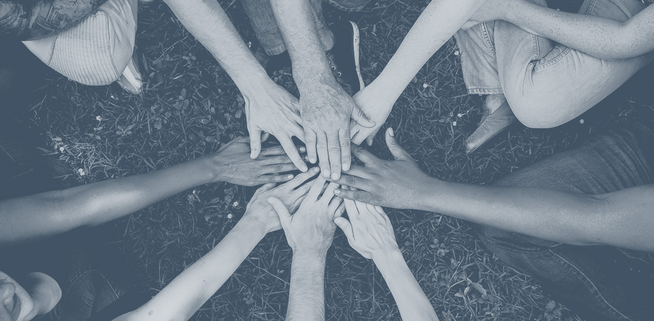 A photo of a diverse set of hands joining in a huddle, overlapping each other towards the center.