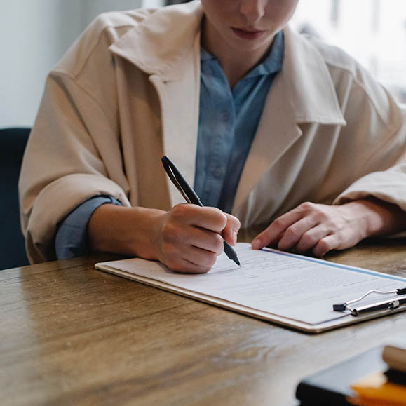 Photo of a woman holding a pen, signing a document on a clipboard.