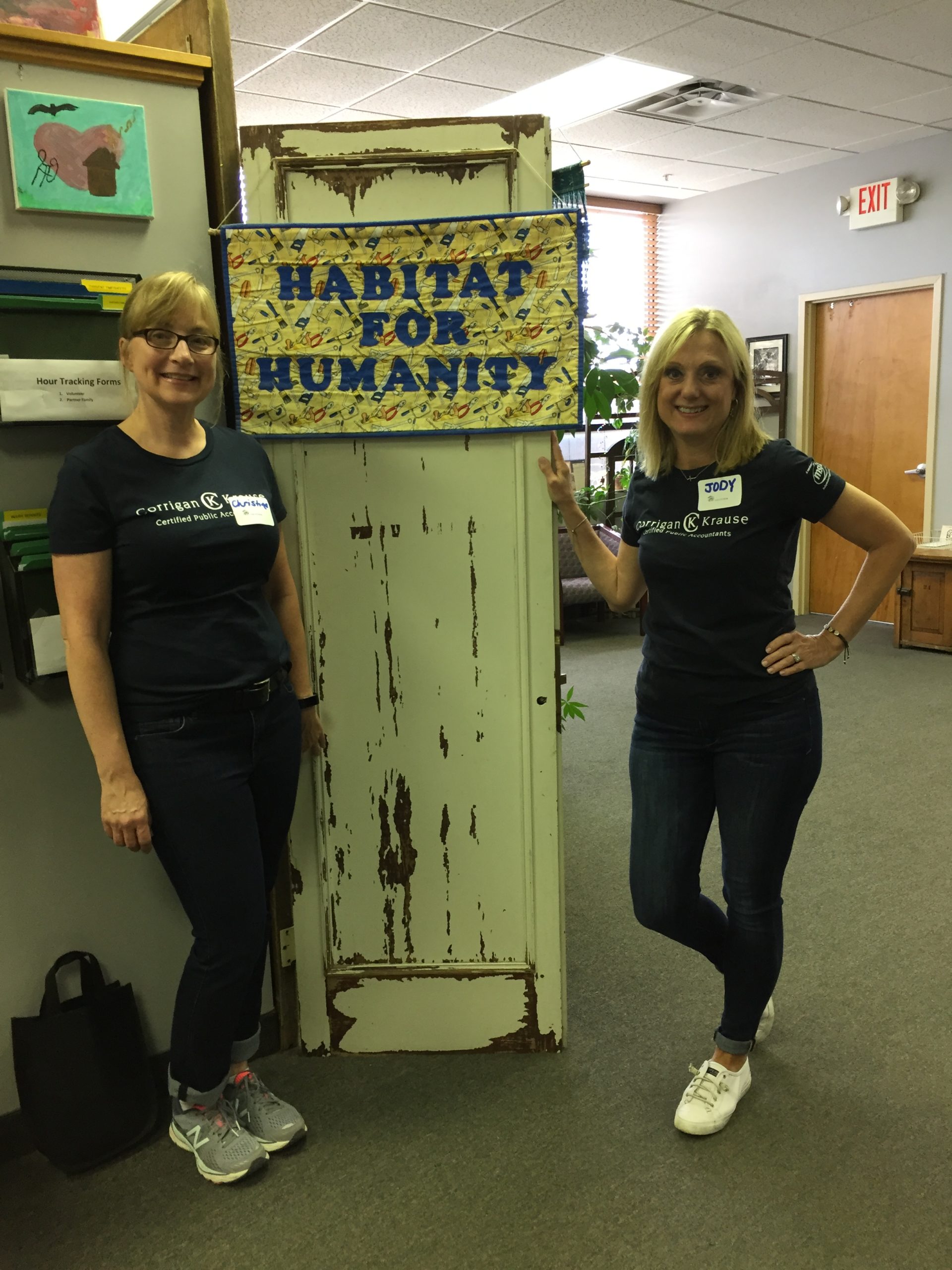 Photo of two women standing in front of a sign that reads "Habitat for Humanity"