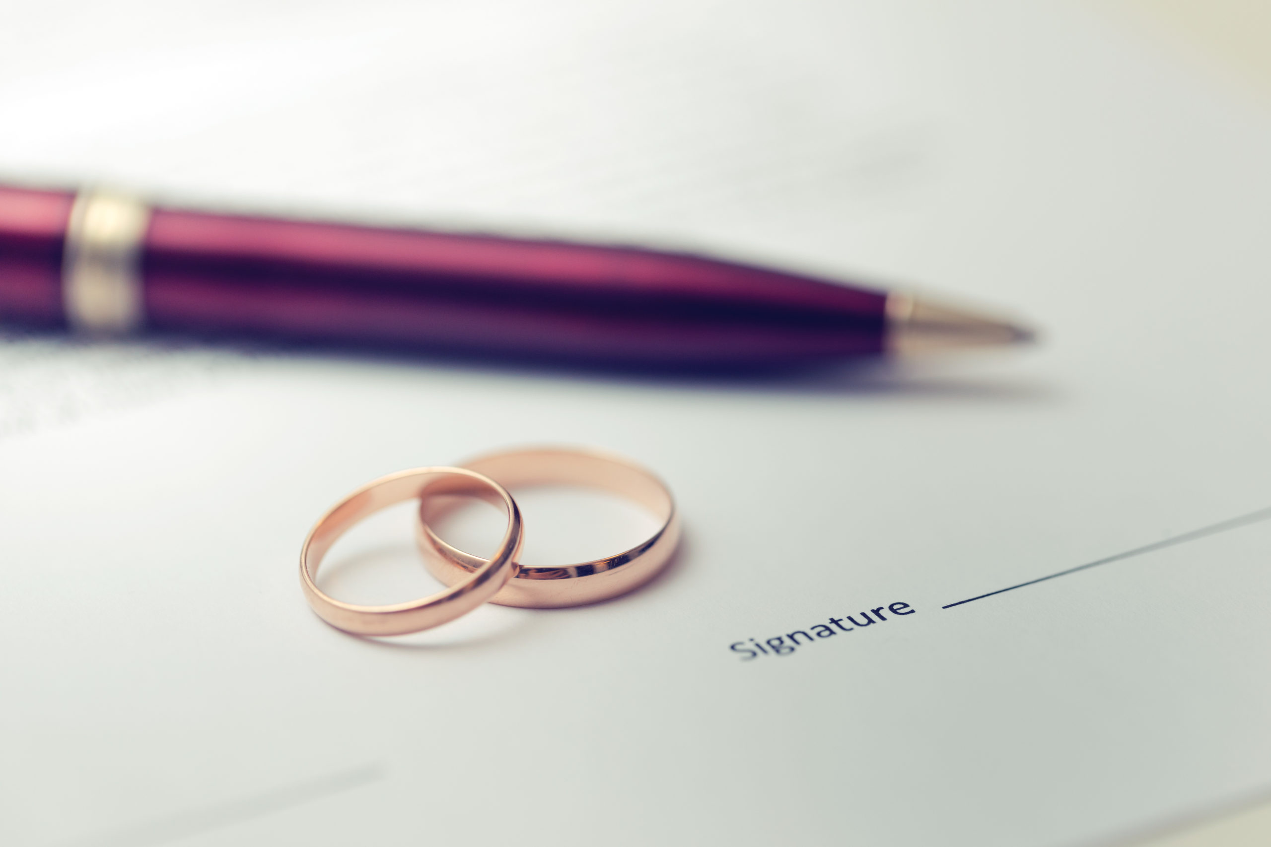 A photo representing a marriage contract, showing a purple pen, laying conveniently next to a signature line, and two stacked wedding rings.