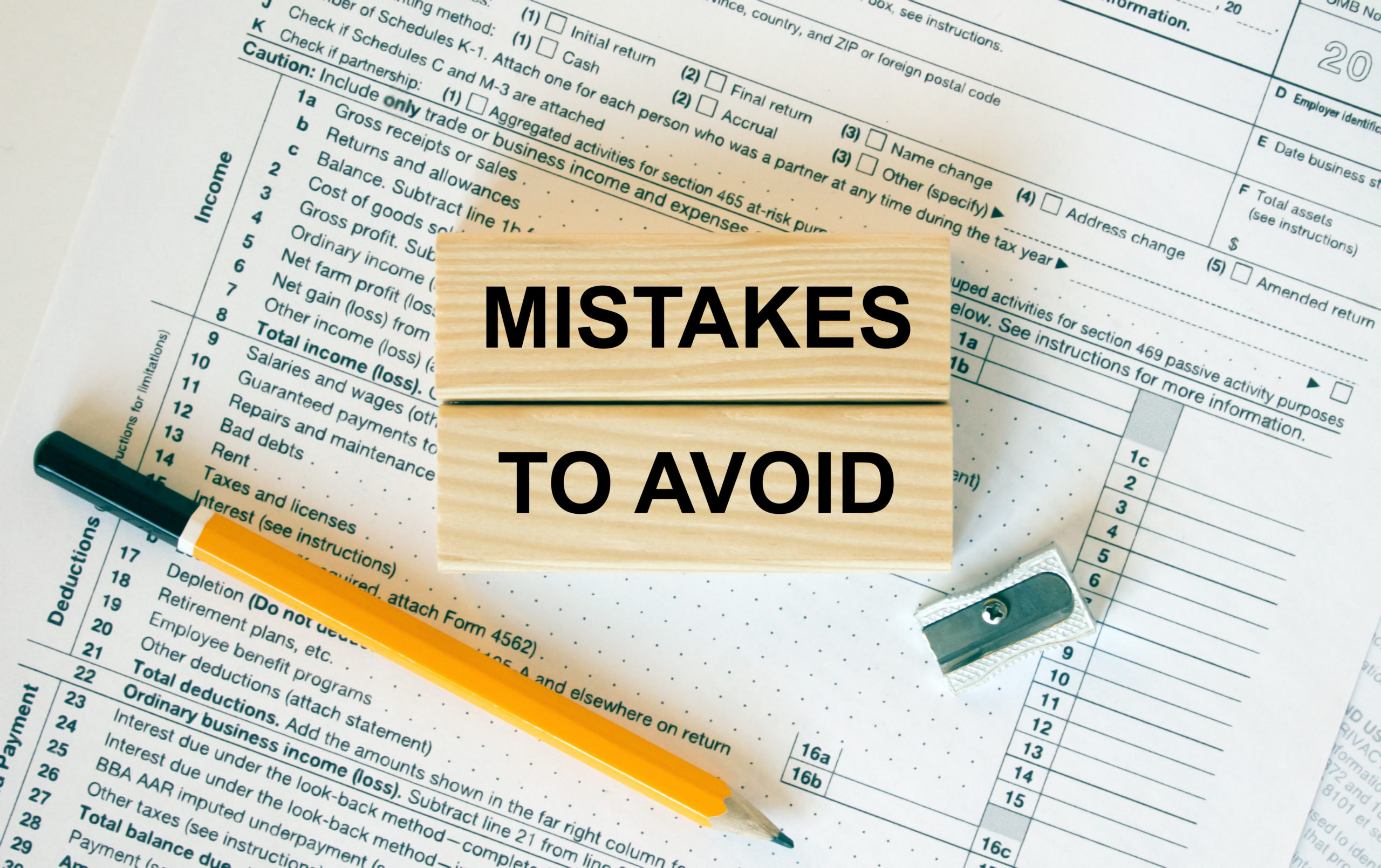 Wooden blocks with the text "Mistakes To Avoid" on them, sitting atop financial documents, with a pencil and pencil sharpener.